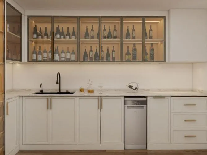 Sink run of white Shaker cabinets with brass pulls under a row of lit glass cabinets with bottles
