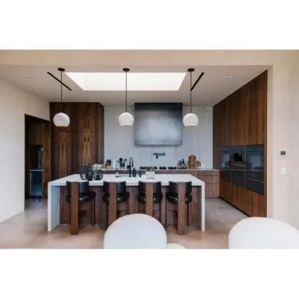 Walnut kitchen with a white waterfall island, leather stools and white globe pendants under a skylight