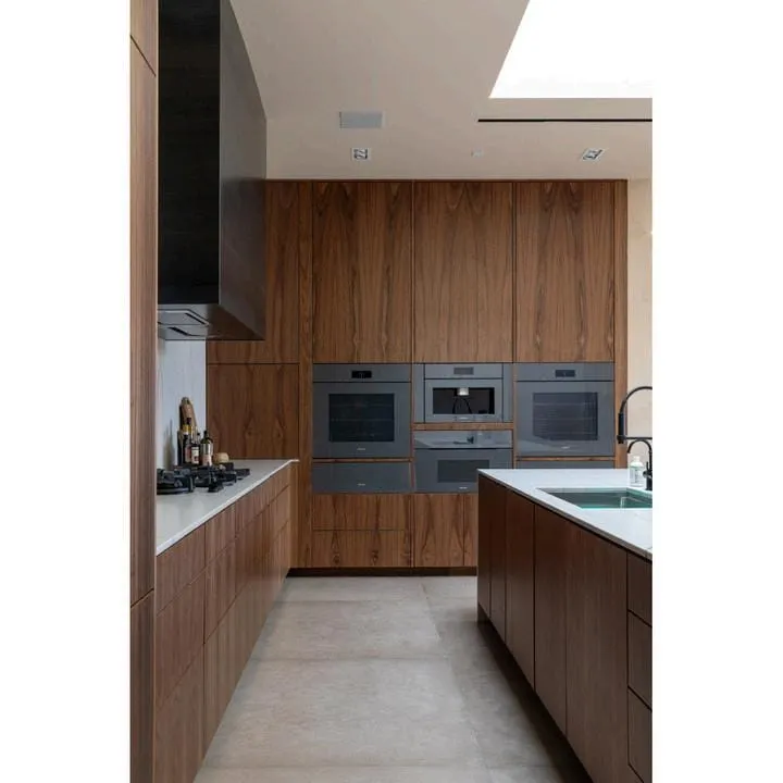 Walnut galley with stacked gray wall ovens, a cooktop and a black hood