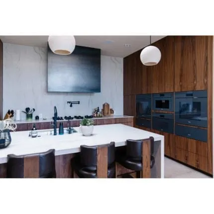 Close view of a white island with black faucet, walnut cabinets and a wall of built-in ovens