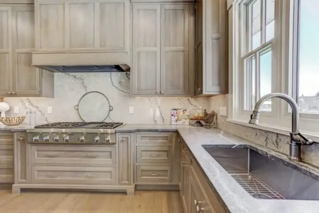 Stainless professional range under a cabinet-wrapped hood with a full-height white marble backsplash