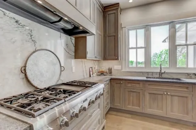 Undermount sink under double-hung windows with oak inset cabinets and marble counters