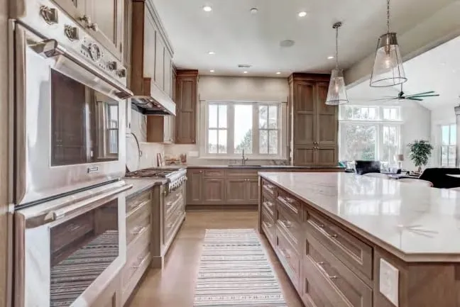 Galley view with double wall ovens, oak cabinets and a marble-topped island