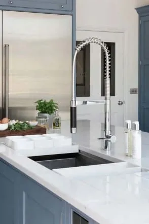 Close view of a stainless pull-down faucet over an undermount sink in a white quartz counter