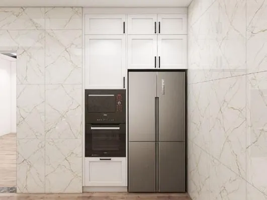 Tall white cabinets with a stainless refrigerator and stacked wall ovens set into marble-look wall slabs