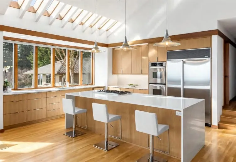 Oak kitchen with a white waterfall island, three white stools, cone pendants and skylights