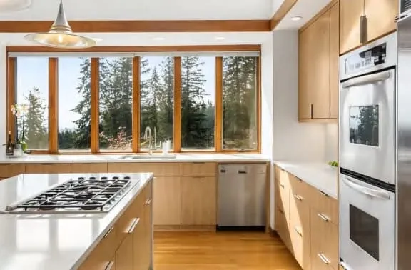 Gas cooktop on a white island facing a band of windows with a view of evergreen trees