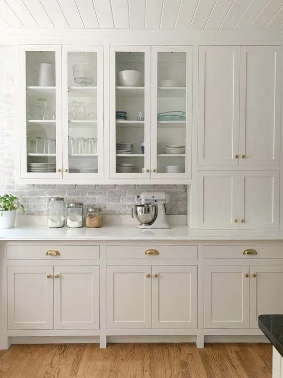 Greige inset cabinets with glass-front uppers, brass cup pulls and a beadboard ceiling