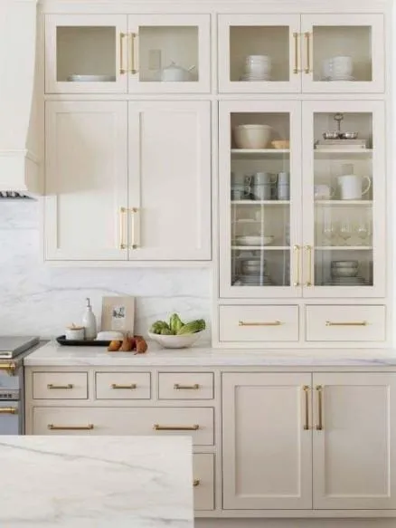 Greige glass-front cabinets with long brass handles and a white marble counter