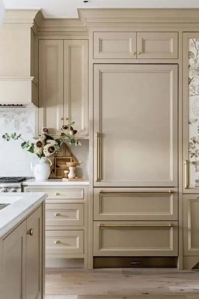Panel-front refrigerator in greige cabinetry with a brass handle and marble counter