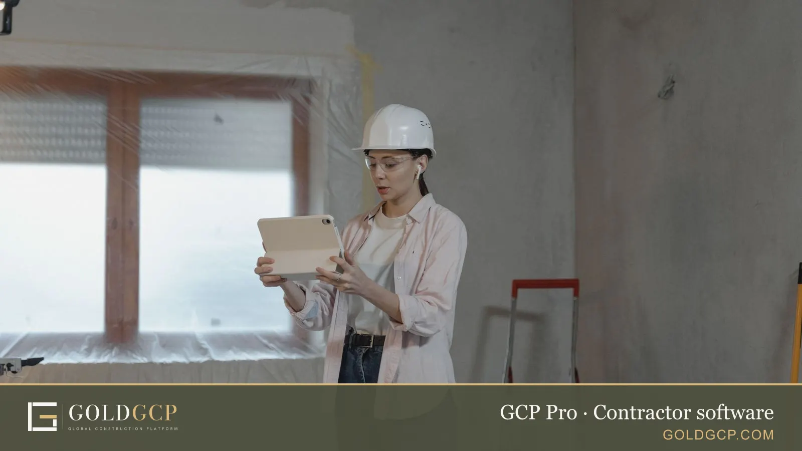 A builder in a hard hat using a tablet inside an unfinished room