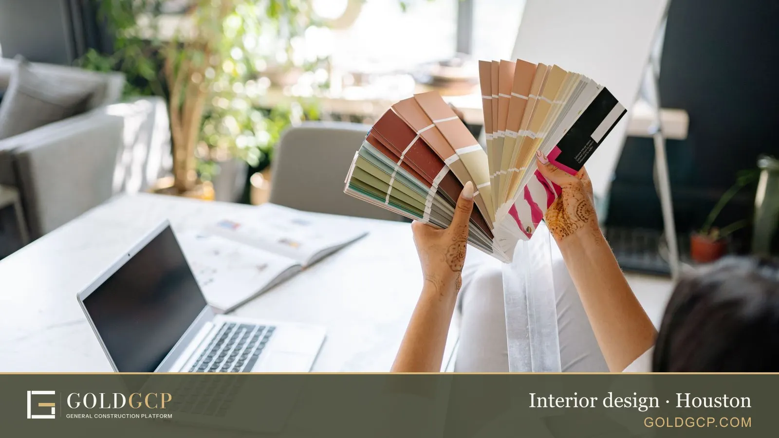 An interior designer compares paint color swatches next to a laptop in a bright room