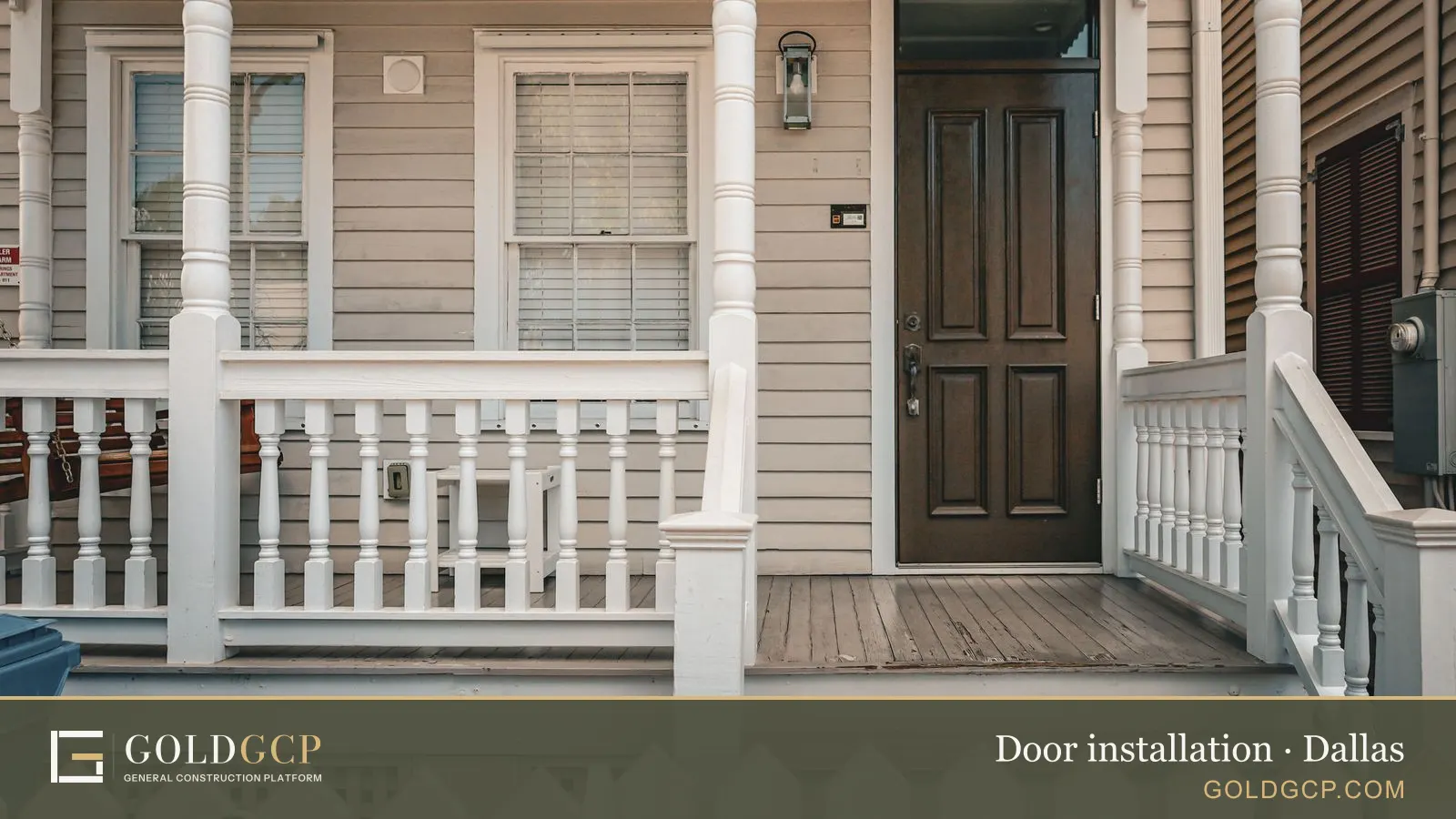 A dark wood paneled front door on a white wooden porch behind a picket fence