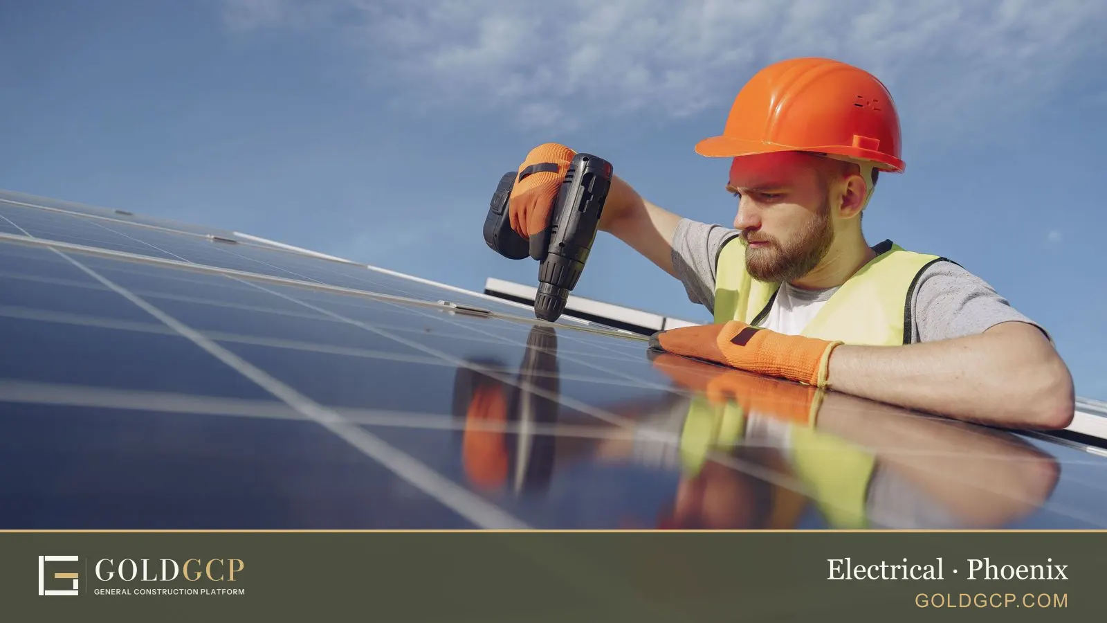 An electrician in a hard hat and gloves installing a solar panel system with a drill