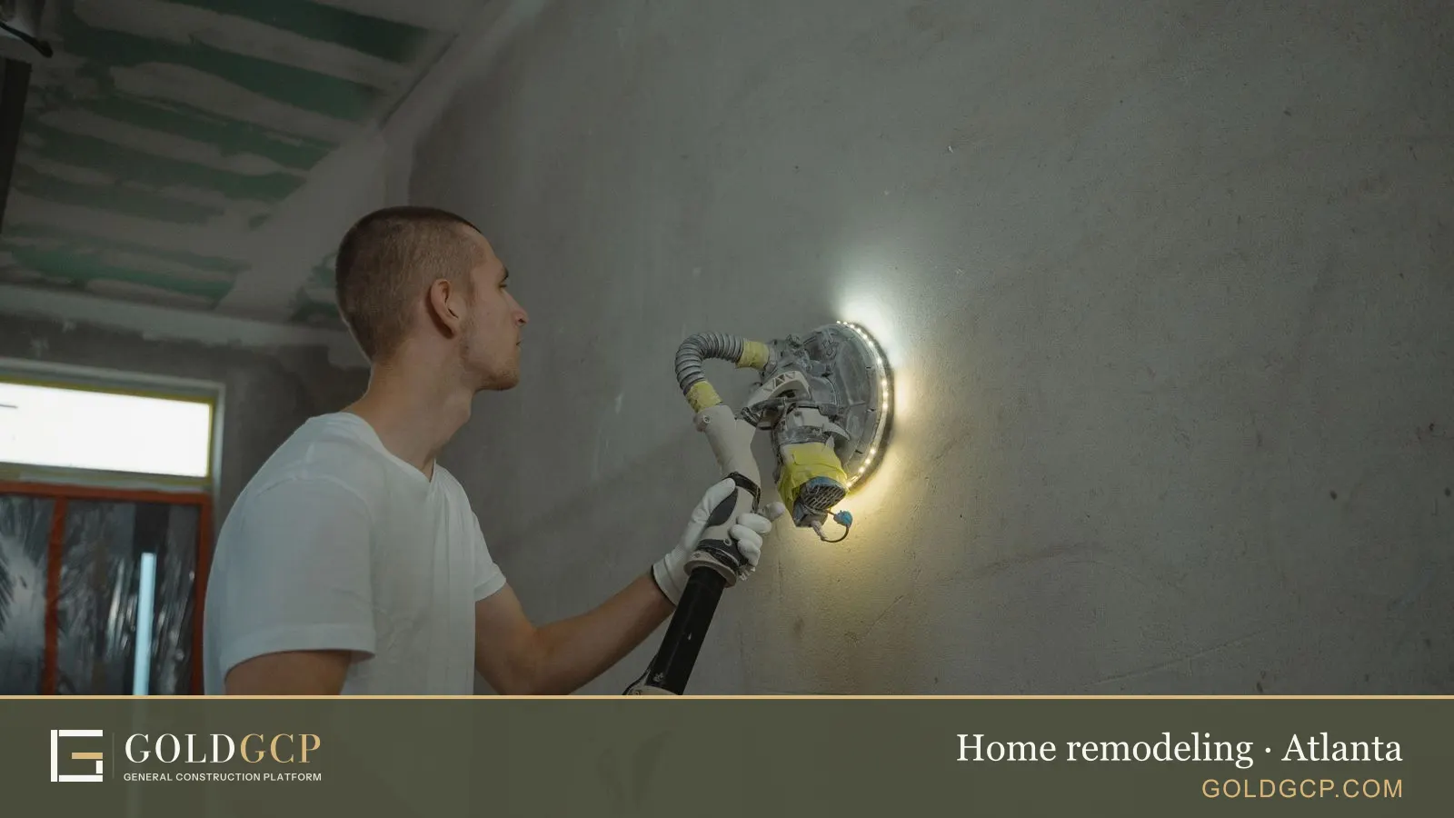 Man using a power tool to sand a wall during an indoor home renovation project.