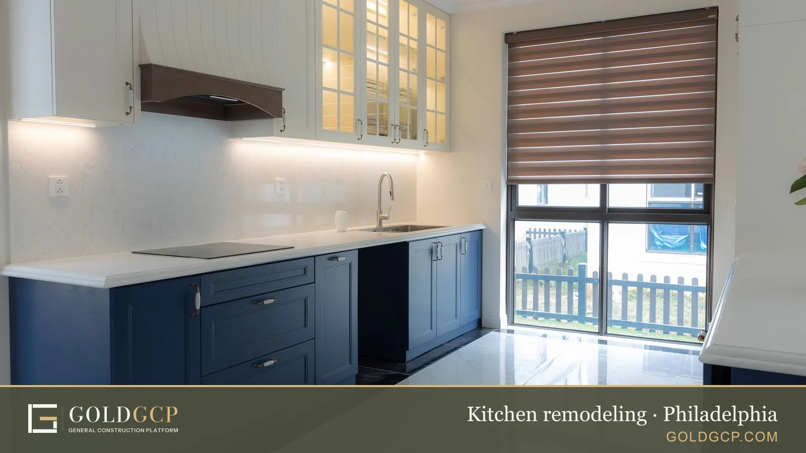 Bright modern kitchen with blue cabinetry, marble countertops, and natural light from large windows.