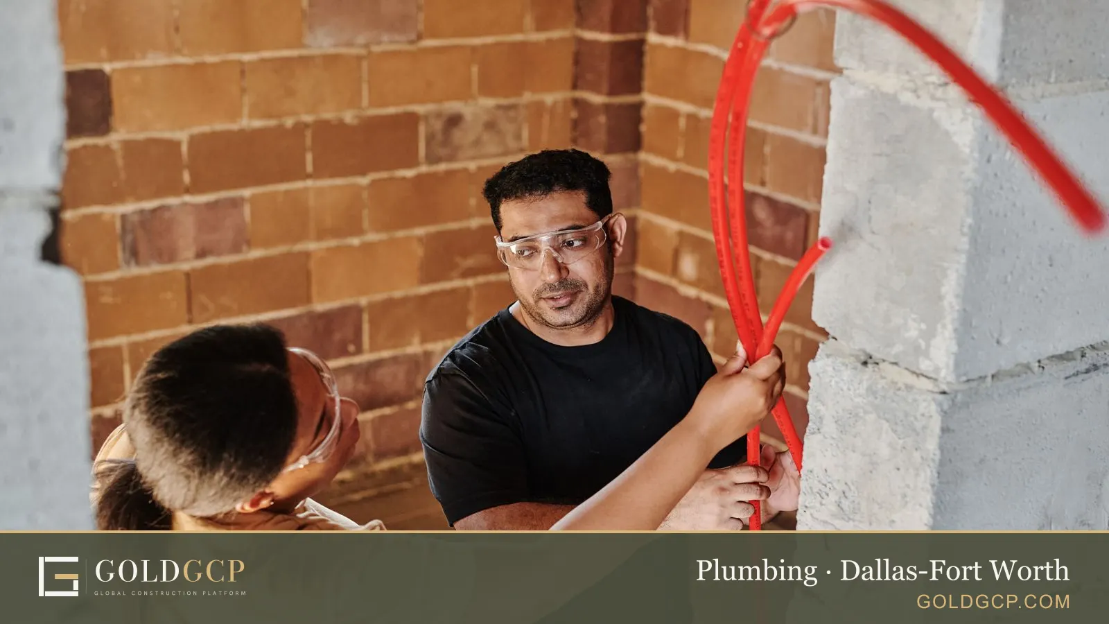 Two workers fitting new red water tubing along a brick wall