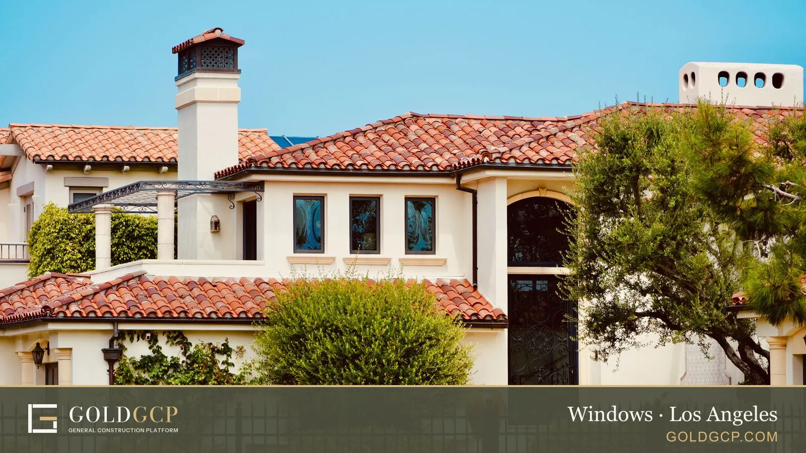 A two-story Spanish style house with a red tile roof and divided-lite windows behind a wrought iron fence
